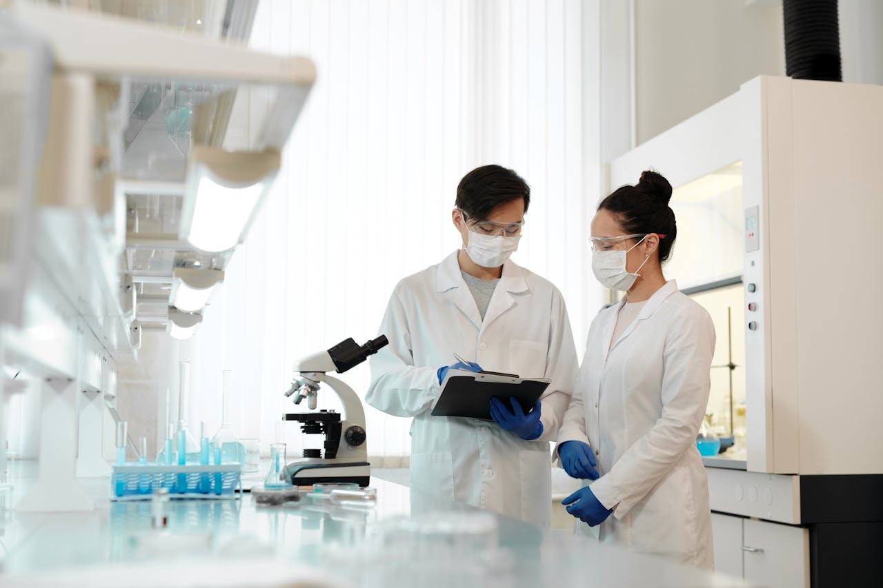 Two scientists in a laboratory wearing masks, discussing research with a microscope.